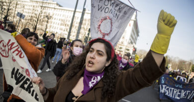 Im Bild: Eine Frau reckt eine Faust in die Höhe, sie trägt Putzhandschuhe. Im Hintergrund ein Schild "Power to the women".