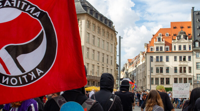 Antifaschistischer Protest steht auf dem Marktplatz in Leipzig, im Hintergrund ist die Demo der "Bewegung Leipzig" zu sehen, bei der eine Reichsflagge weht