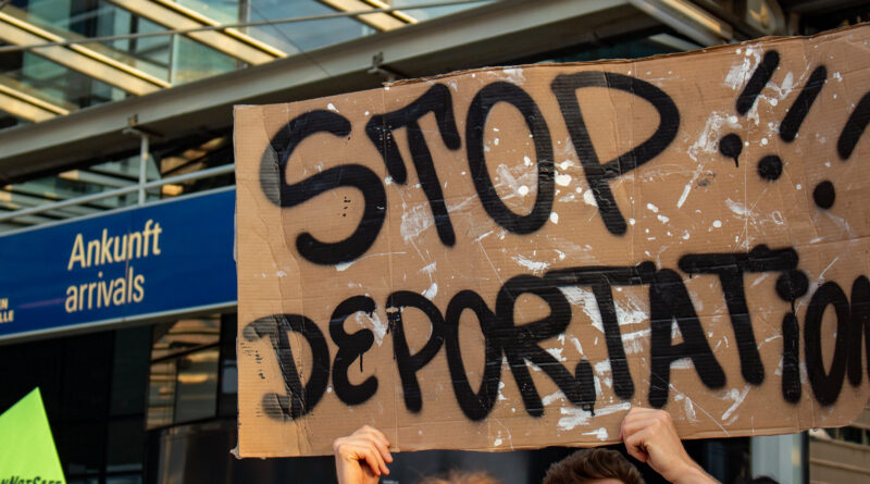 Beim Protest gegen die Abschiebung am Leipiger Flughafen hält eine Person ein Schild mit der Aufschrift "Stop Deportation" vor dem Ankunftsterminal in die Höhe