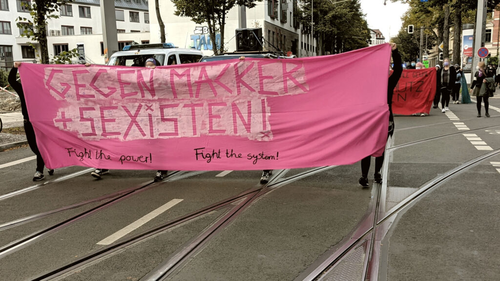 Foto des Fronttransparents: "Gegen Macker und Sexisten - Fight the power fight the system"